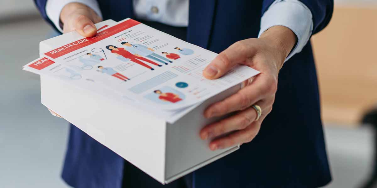 A person holding a stack of full color printed flyers.